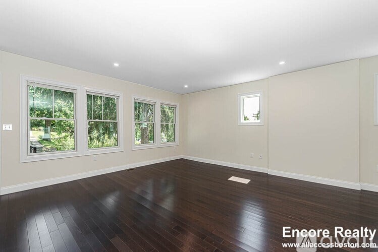 A spacious room with wooden floors and three windows.