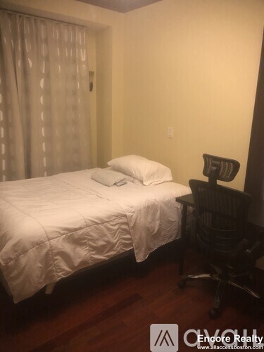 A bedroom with a bed, chair, and a window with curtains.