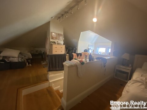 A bedroom with a bed on the left and a desk with a lamp on the right.