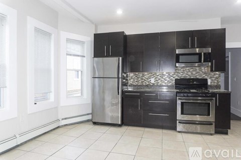 A kitchen with black cabinets and a stainless steel refrigerator.