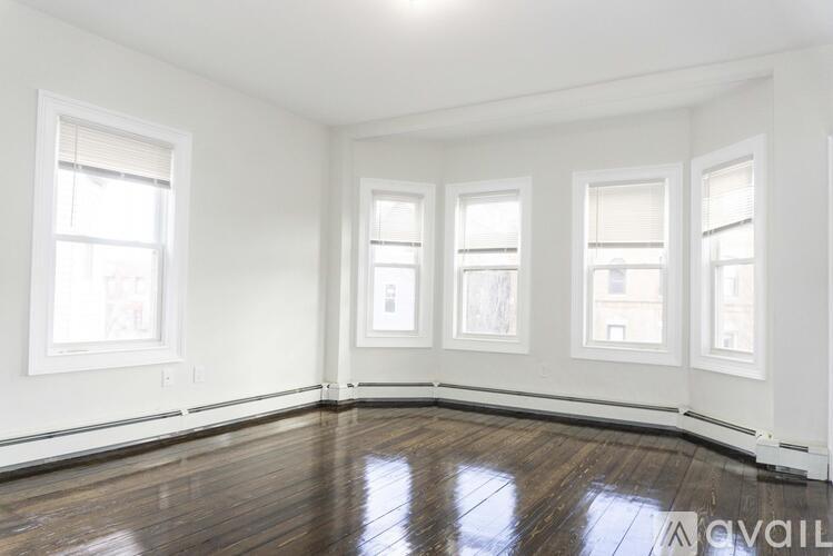 A room with white walls and wooden flooring, featuring four windows.