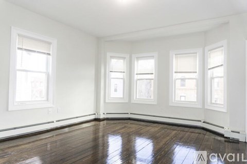 A room with white walls and wooden flooring, featuring four windows.