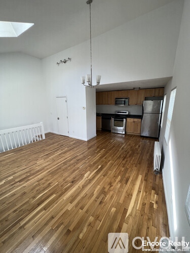 A room with wooden floors and a kitchen area in the background.