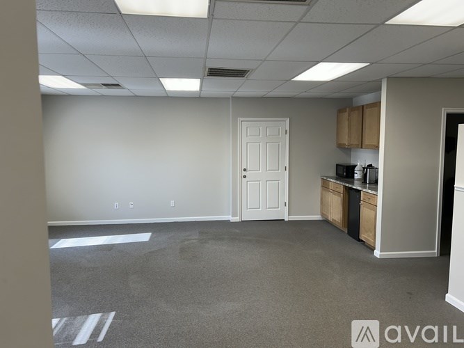 A spacious office room with a white door and cabinets on one side.