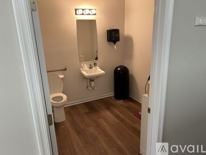 A bathroom with a toilet, sink, mirror, and trash can.