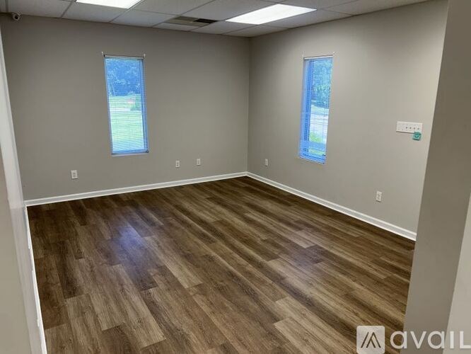 A room with wooden flooring and two windows.