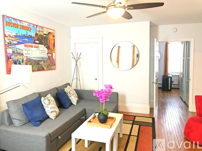 A living room with a grey couch, a white coffee table, a ceiling fan, and a poster on the wall.