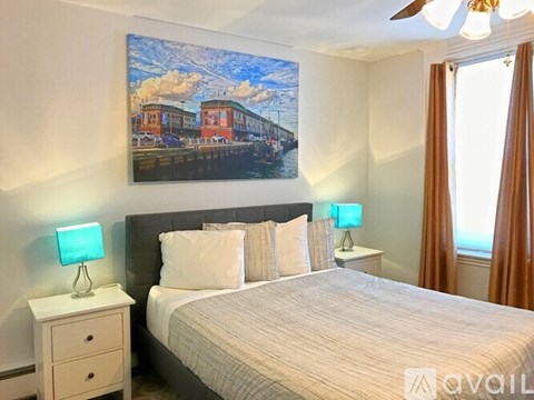 A bedroom with a bed, two lamps, and a painting on the wall.