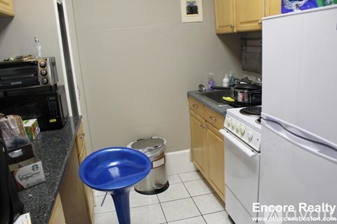 A kitchen with a white refrigerator, a blue stool, and a white oven.