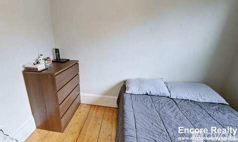 A bedroom with a bed, a wooden dresser, and a nightstand.