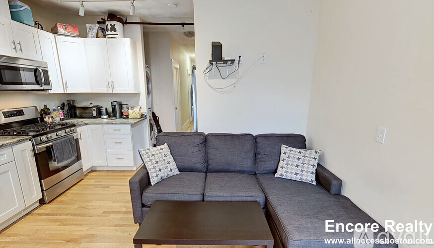 A grey couch with two pillows sits in a kitchen with white cabinets.