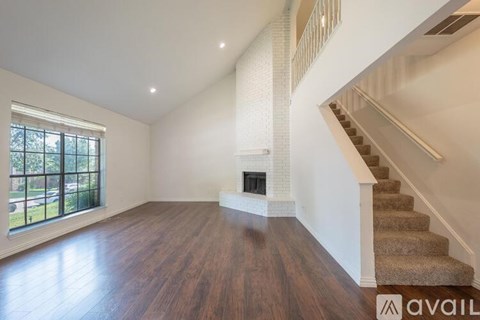 A spacious room with wooden floors and a staircase leading to the upper level.