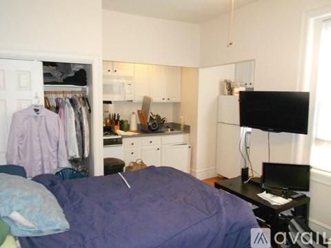 A bedroom with a bed, a television, and a kitchen area.