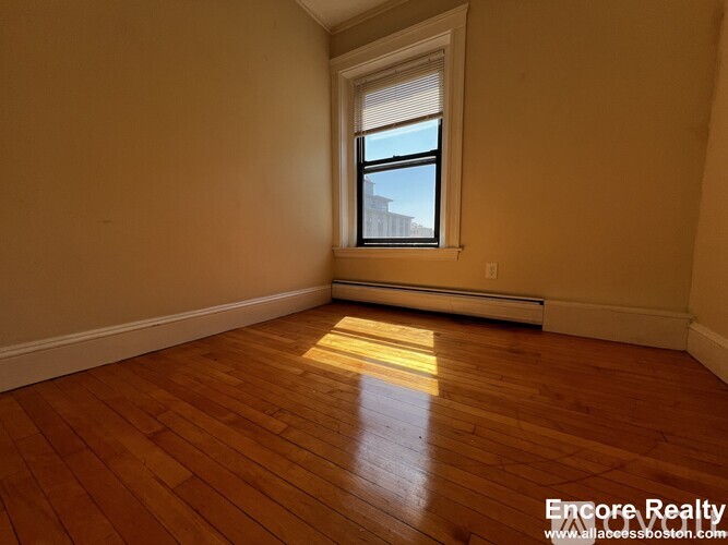 A room with wooden floors and a window letting in sunlight.