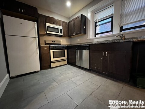 A kitchen with a white fridge, black countertops, and brown cabinets.