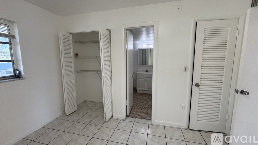 A room with white walls and a tiled floor with a door open to a bathroom.