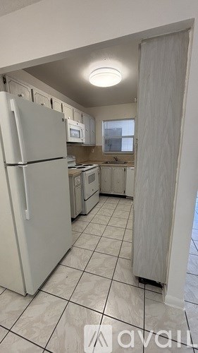A kitchen with a white refrigerator and white tiled floor.