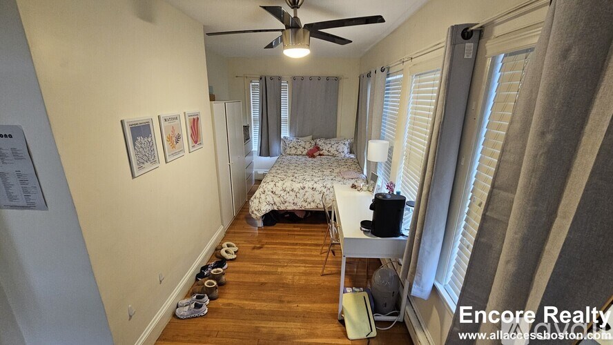 A room with a bed, a desk, and a ceiling fan.
