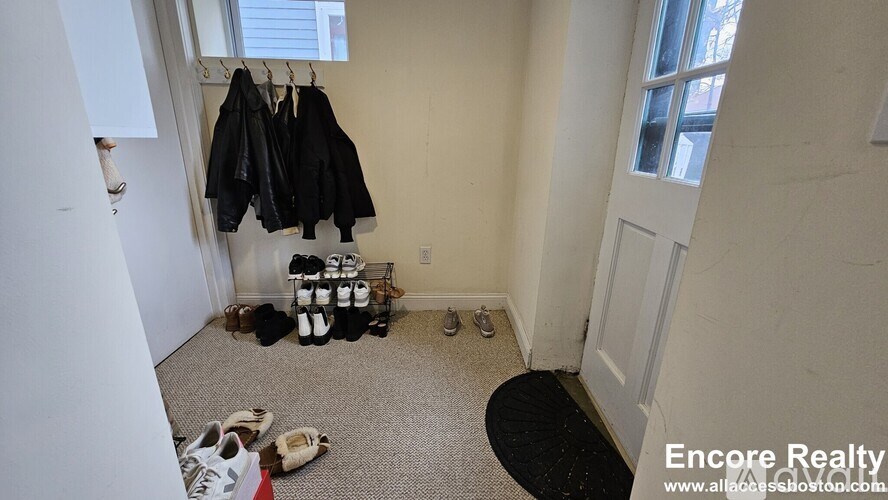 A room with a carpet, a pair of shoes, a jacket and a pair of sneakers hanging on a wall.