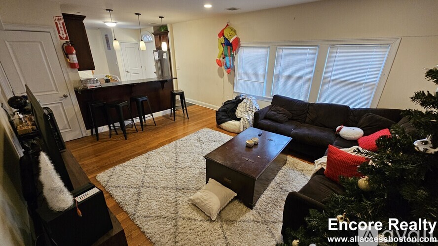 A living room with a Christmas tree and a dining area in the background.