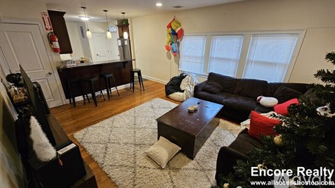 A living room with a Christmas tree and a dining area in the background.