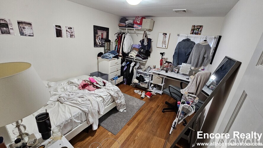 A bedroom with a bed, desk, and clothing rack.
