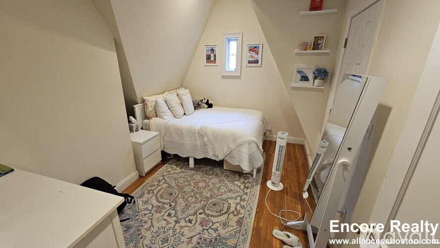A bedroom with a bed, a rug, a dresser, and a fridge.