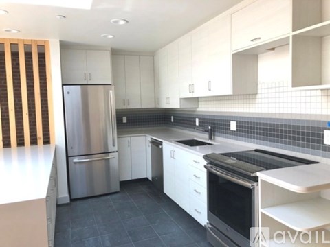 A kitchen with a stainless steel refrigerator and black countertops.