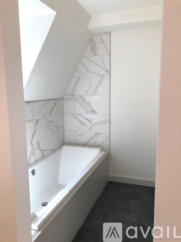 A bathroom with a marble patterned wall and a white bathtub.