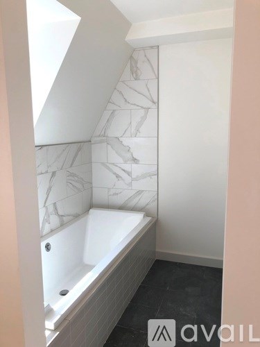 A bathroom with a marble patterned wall and a white bathtub.