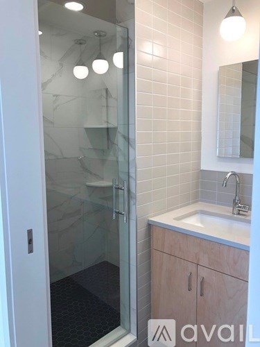 A bathroom with a glass shower door and a sink with a cabinet under it.
