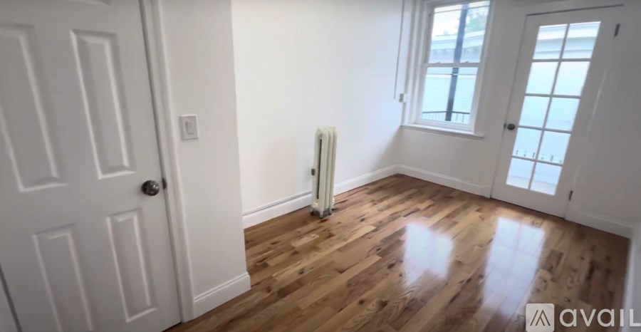 A room with a white door, a window, and a radiator on the wall.