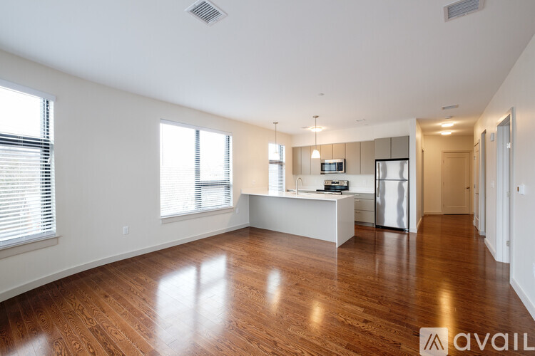 A spacious living room with hardwood floors and a kitchen area in the background.