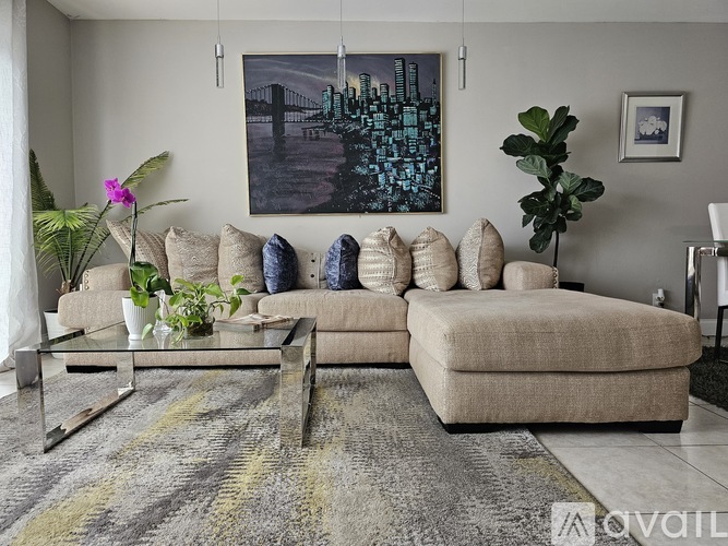 A living room with a beige sofa, a glass coffee table, and a large painting on the wall.
