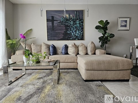 A living room with a beige sofa, a glass coffee table, and a large painting on the wall.