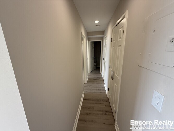 A long hallway with white walls and wood flooring.