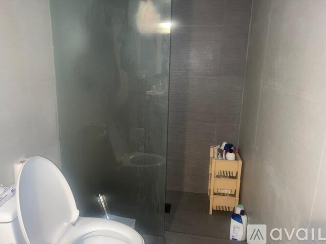 A bathroom with a toilet, a glass shower door, and a wooden crate on the floor.