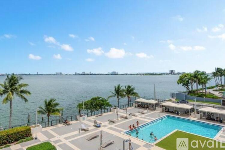 A pool area with a view of the water and palm trees.