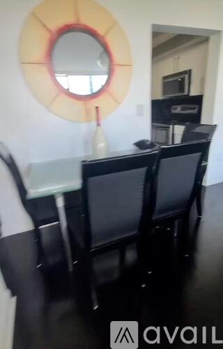 A round mirror with a red outline hangs on a white wall above a black table with two chairs.