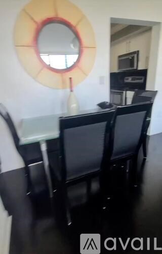 A round mirror with a red outline hangs on a white wall above a black table with two chairs.