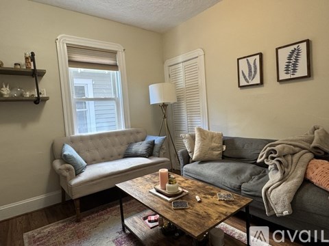 A living room with a grey couch, a wooden coffee table, and a window with white blinds.