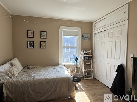 A bedroom with a bed, a window, a door, and pictures on the wall.