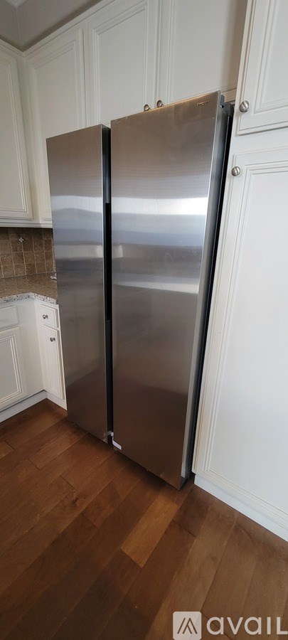 A stainless steel refrigerator in a kitchen with wooden flooring.