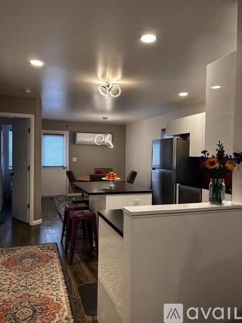 A kitchen with a refrigerator, a dining table with chairs, and a vase of flowers on the counter.