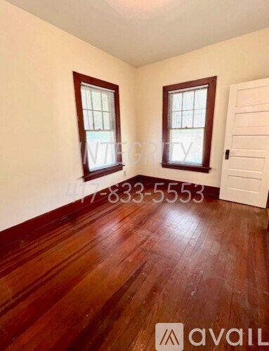 A room with wooden floors and two windows with a white door in the background.