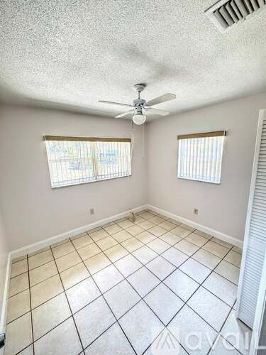 A room with a ceiling fan and two windows.