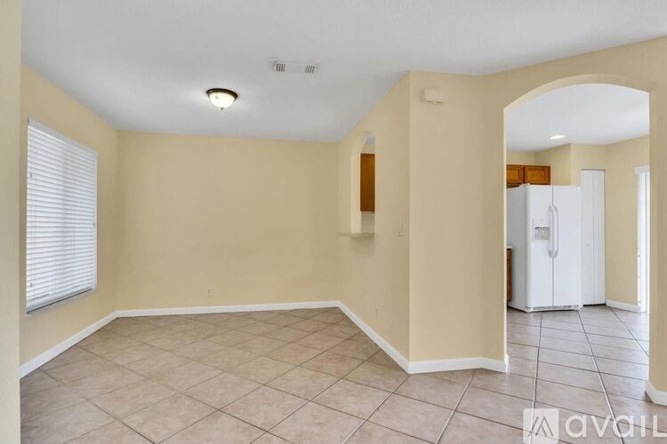 A spacious room with beige walls and a white refrigerator in the corner.