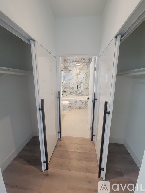 A hallway with a white wall and a wooden floor leading to a bathroom.