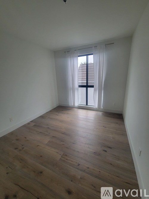 A room with wooden flooring and a window with white curtains.