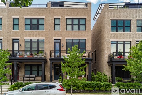 A row of brown brick apartment buildings with balconies and a car parked in front.